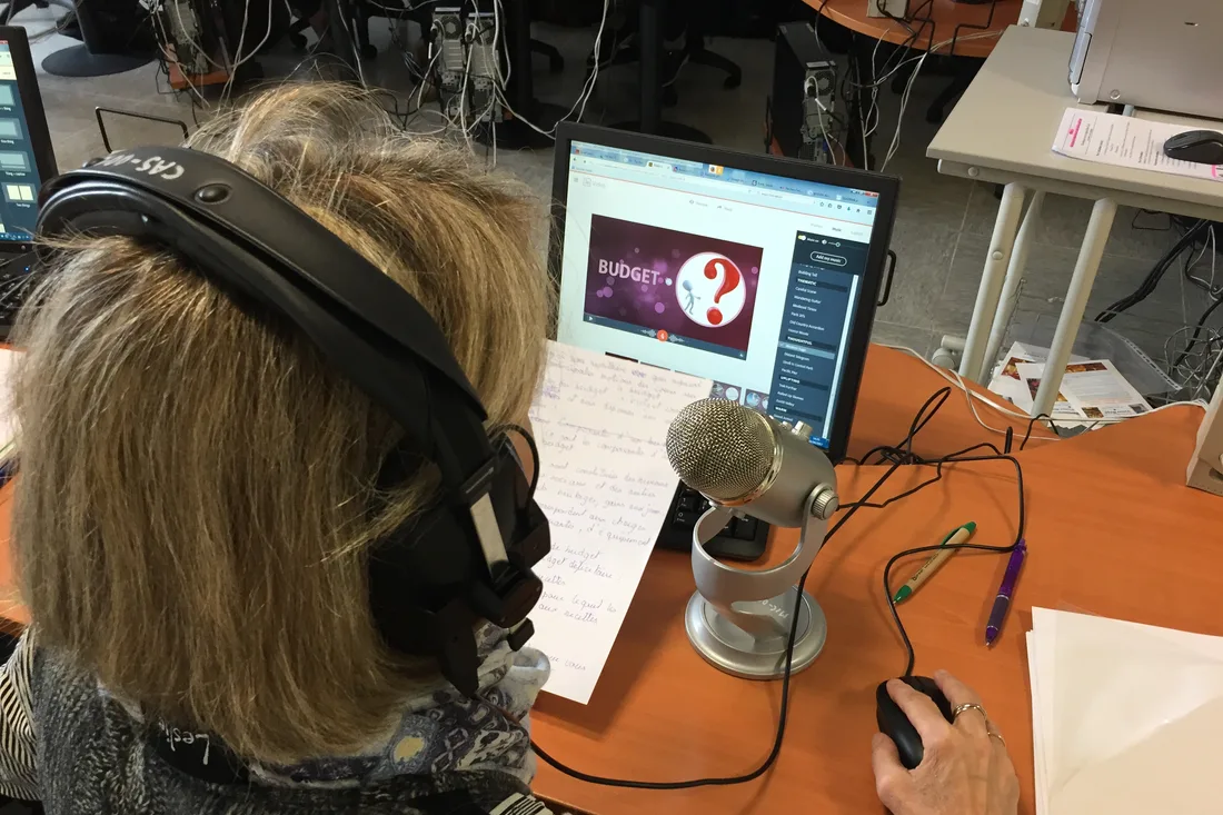 A person wearing headphones recording a podcast, speaking into a desktop microphone in front of a computer