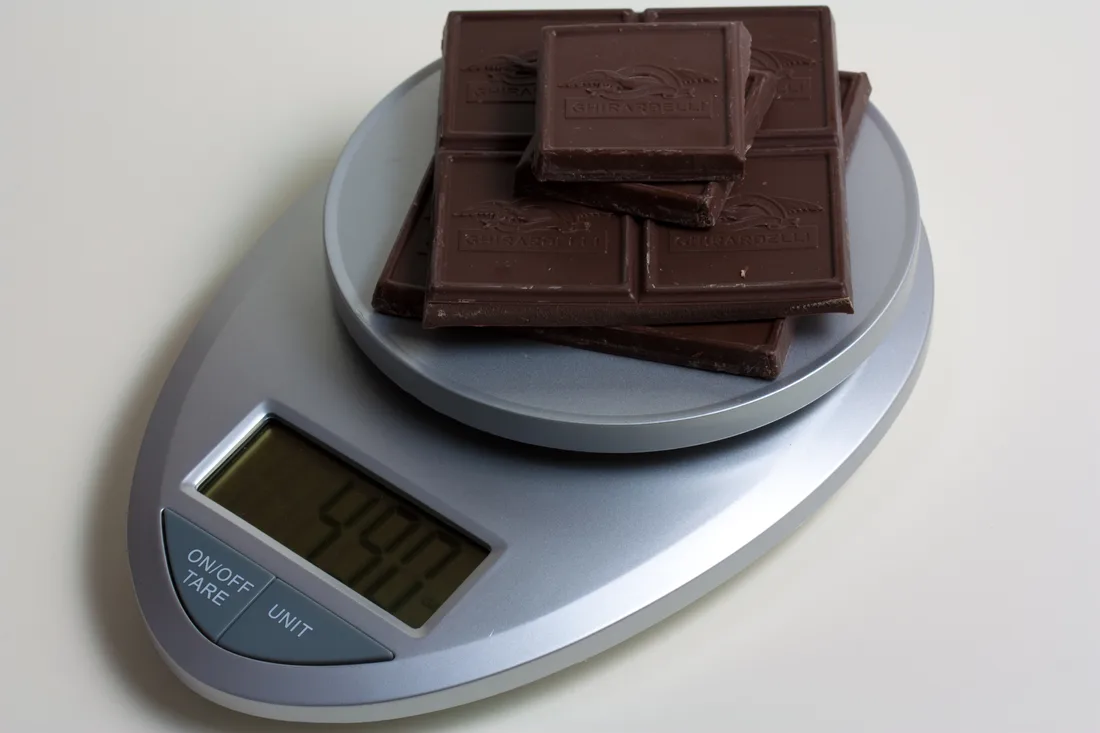 A digital kitchen scale weighing several squares of chocolate, with the weight shown in grams on its display